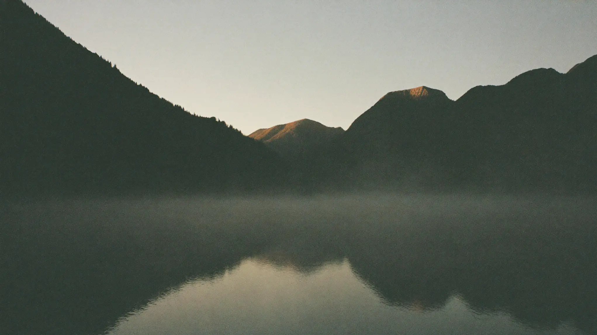 Nebel über einem stillen See im Morgenlicht.