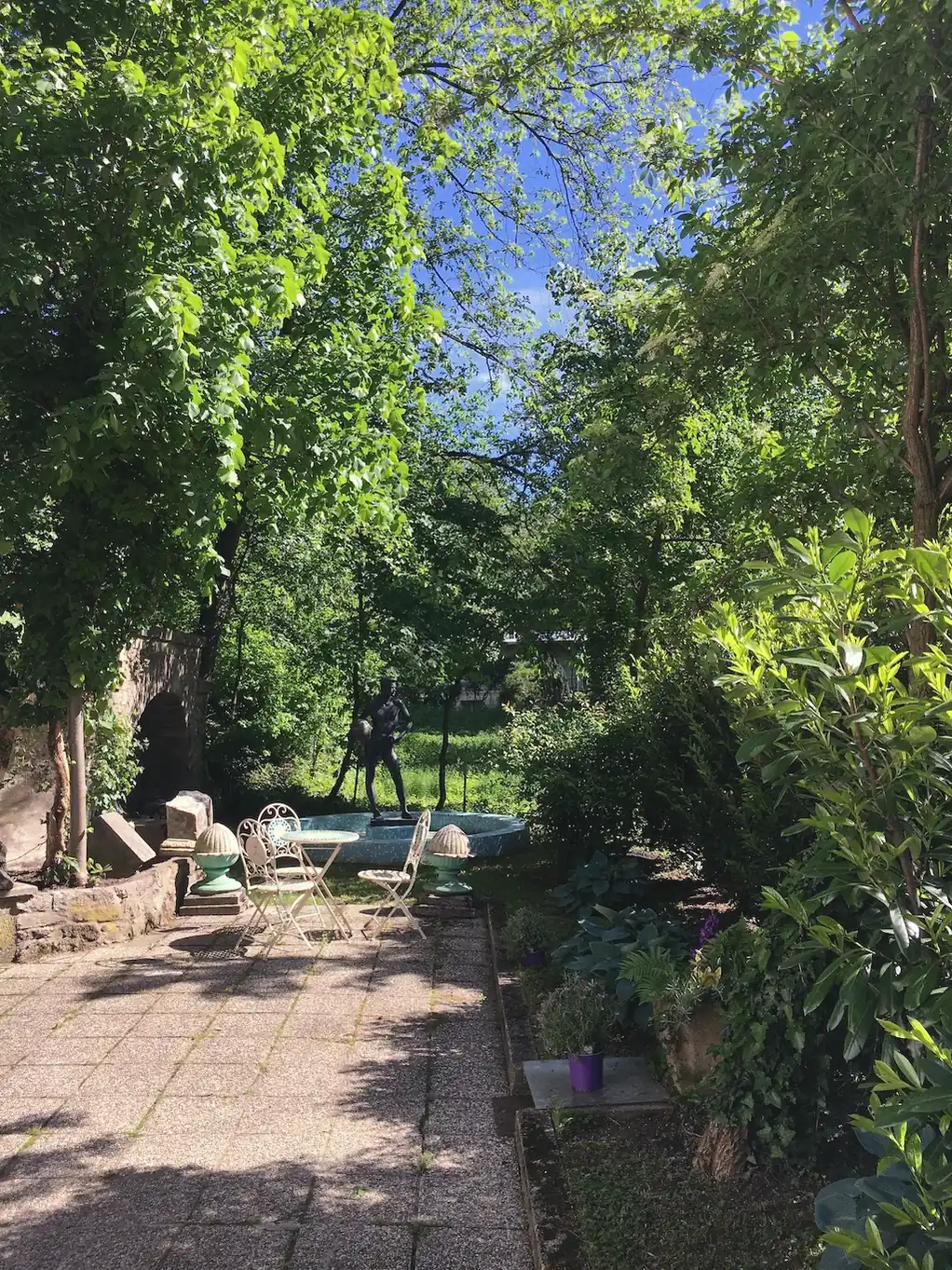 Ein Gartenweg unter hohen Bäumen im Sommerlicht.
