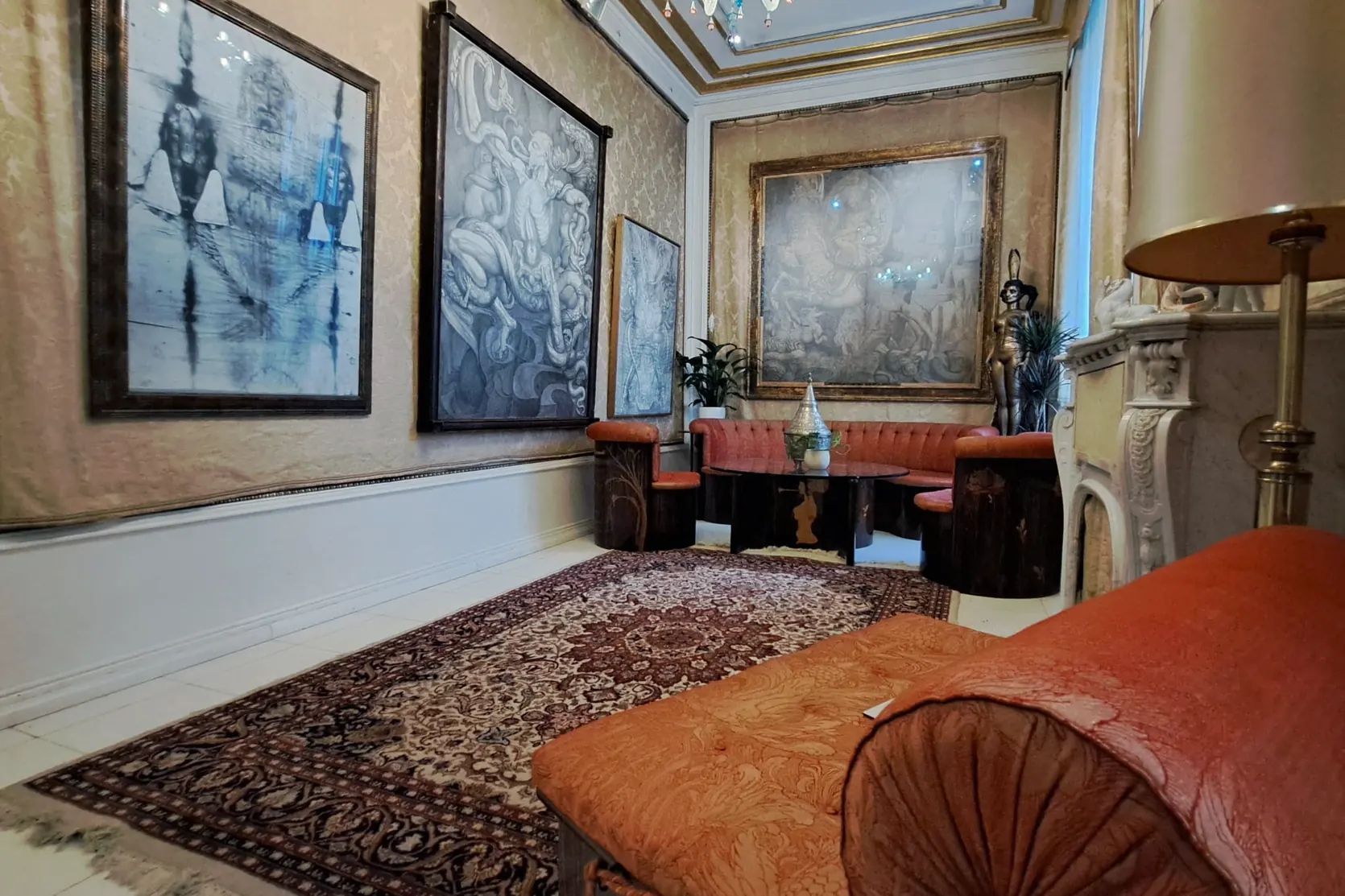 Ein Salon der Villa mit großformatigen Gemälden, rotem Sofa und Kamin.